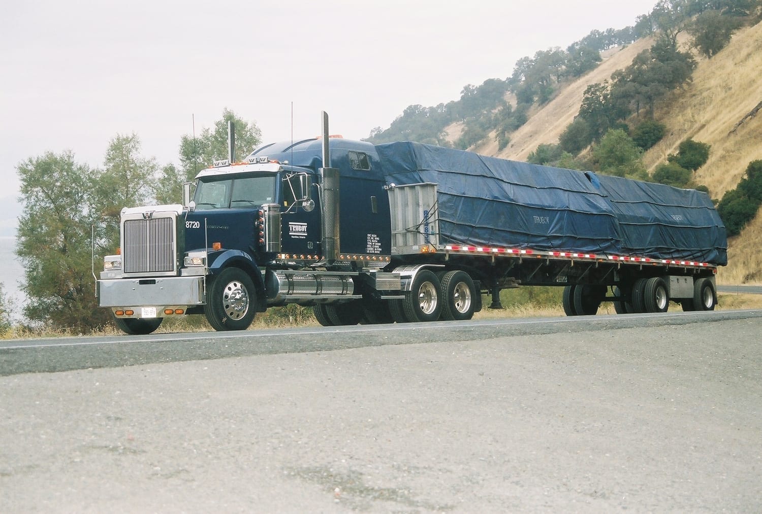 Western Star sleeper with a fully tarped flatbed load on a mountain highway